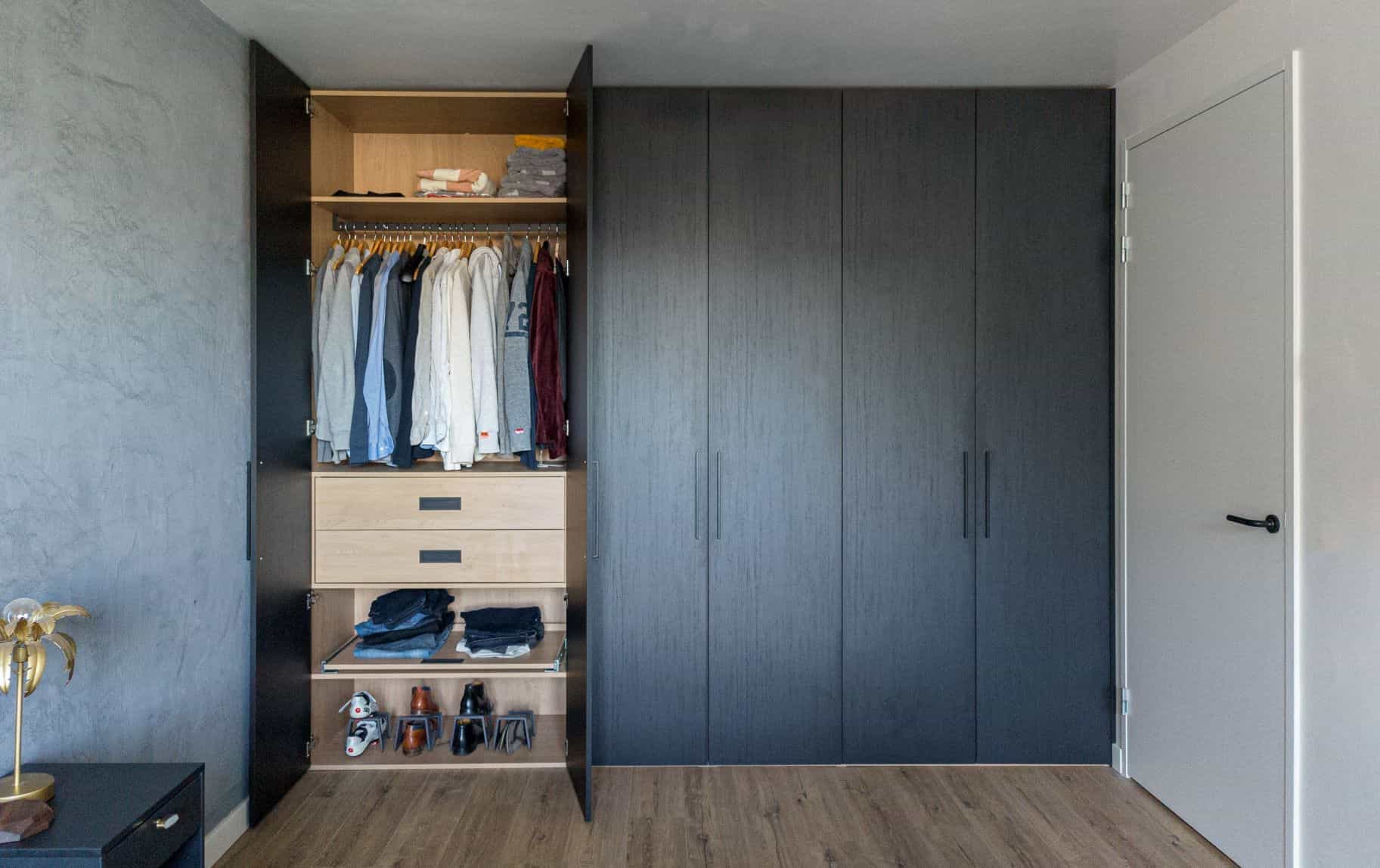 Strakke zwarte kledingkast met hangruimte, planken en lades in een slaapkamer in Blaricum.