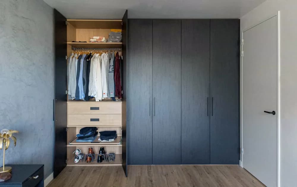 Strakke zwarte kledingkast met hangruimte, planken en lades in een slaapkamer in Blaricum.