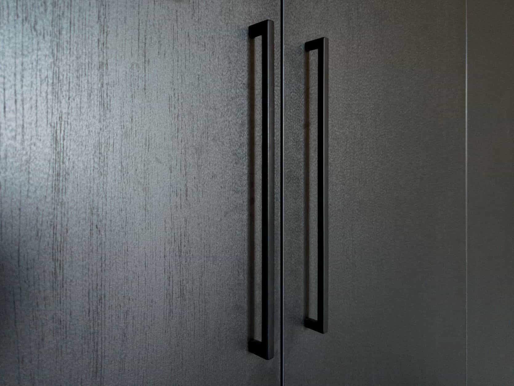Close-up van de handgrepen op een zwarte kledingkast met houtdecor in een slaapkamer in Blaricum.