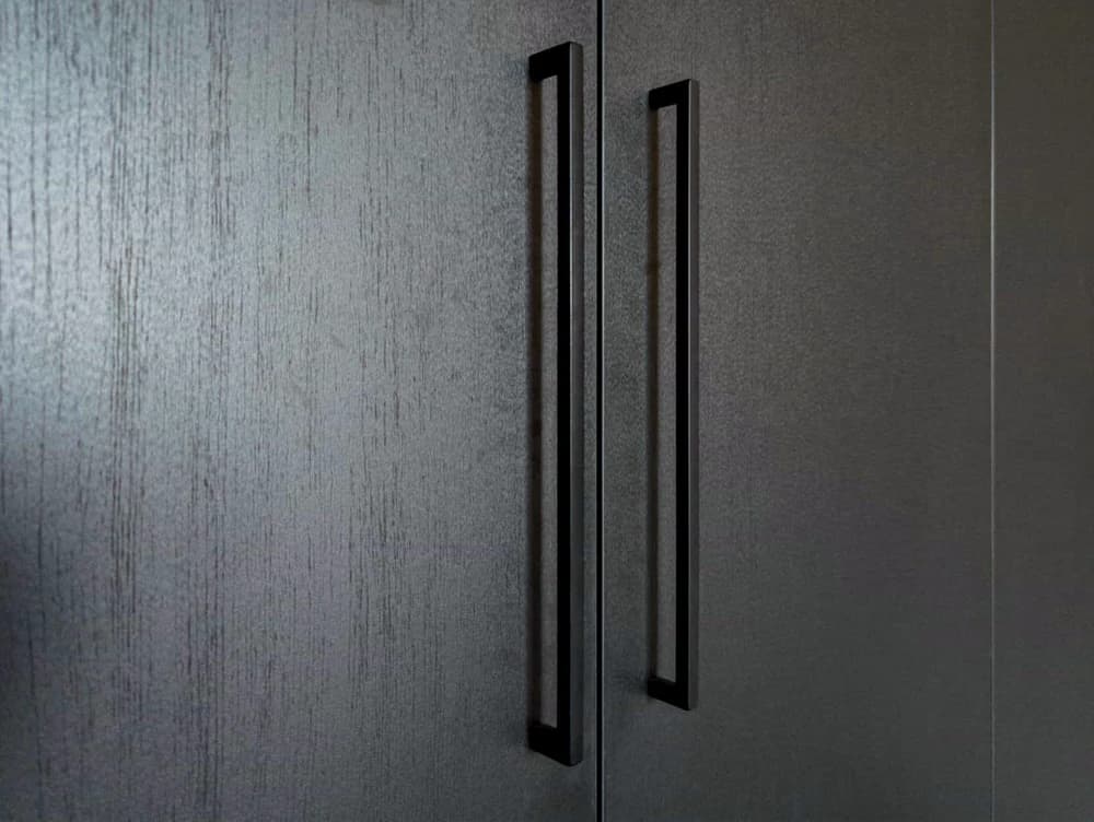 Close-up van de handgrepen op een zwarte kledingkast met houtdecor in een slaapkamer in Blaricum.