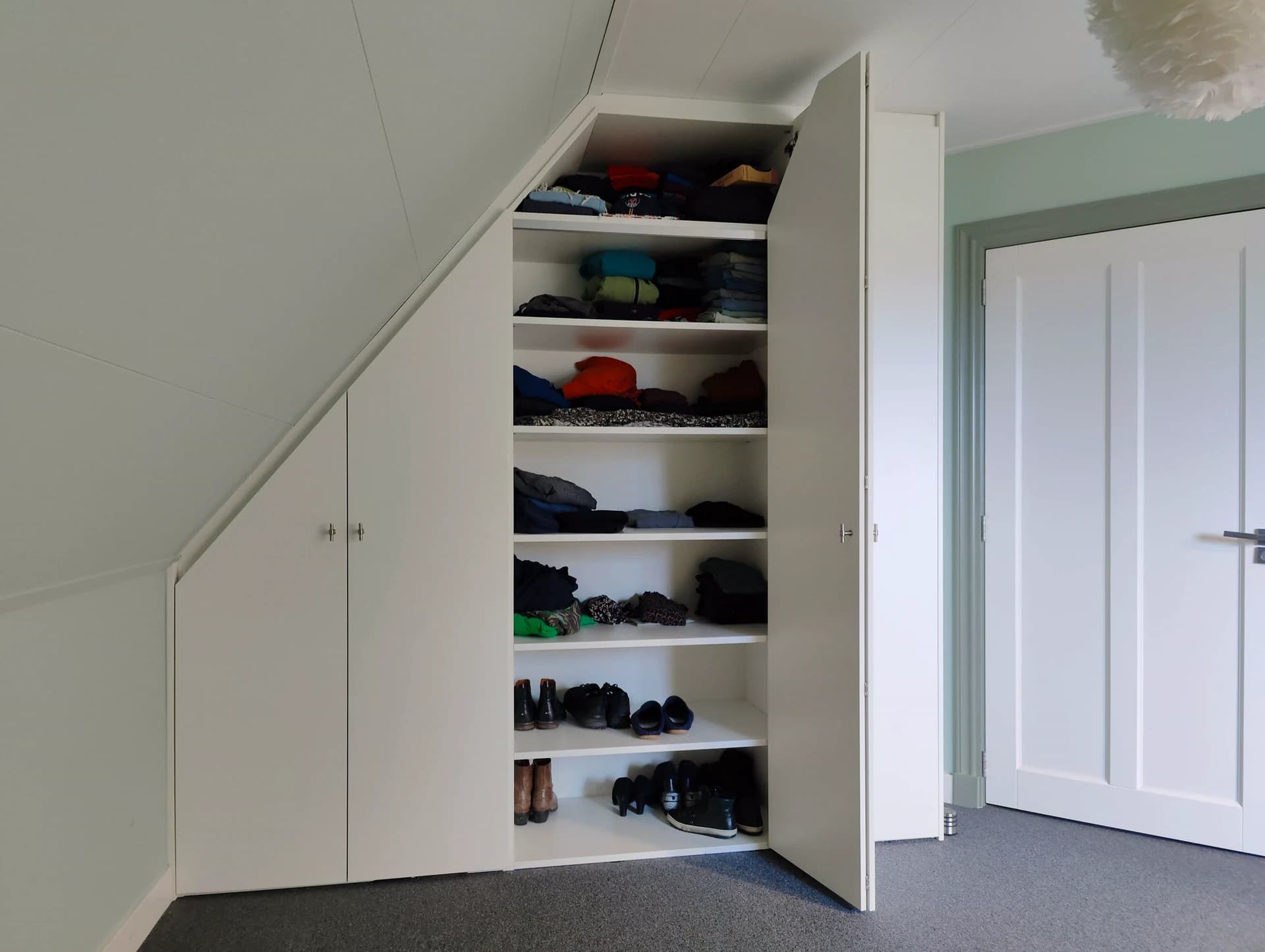 Binnenkant van op maat gemaakte kledingkast onder schuin dak.