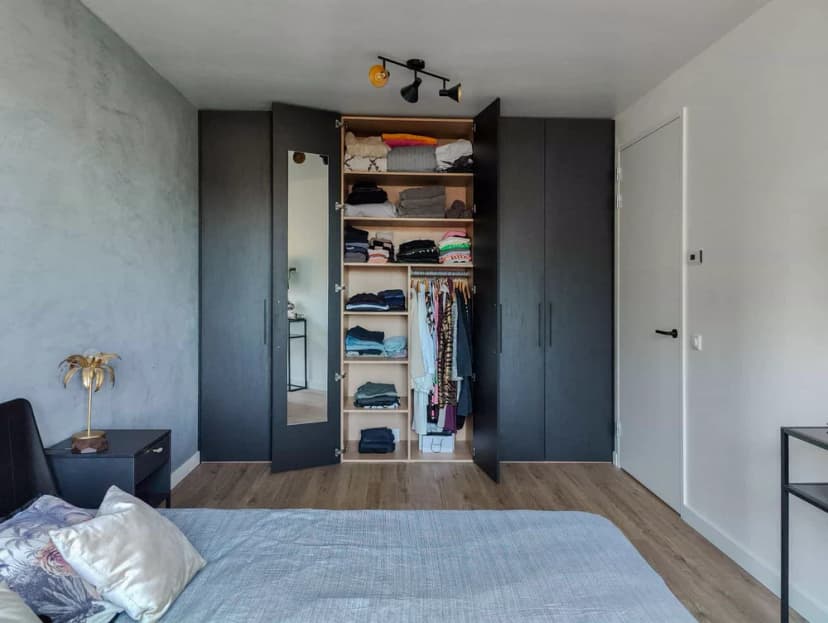 Ingebouwde zwarte kledingkast met open deuren en georganiseerd interieur in een slaapkamer in Blaricum.
