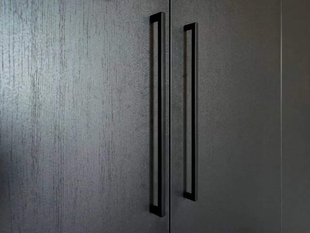 Close-up van de handgrepen op een zwarte kledingkast met houtdecor in een slaapkamer in Blaricum.