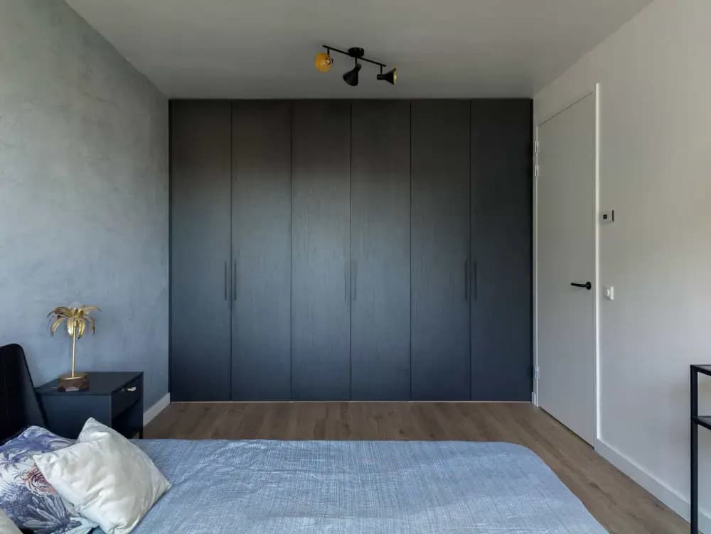 Wandvullende zwarte kledingkast met gesloten deuren in een strakke slaapkamer in Blaricum.