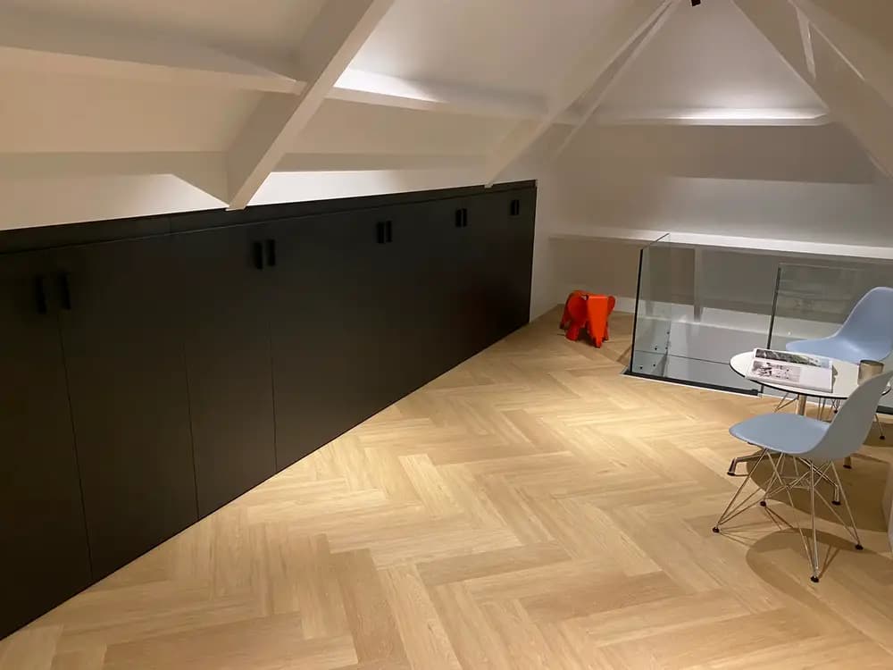 Moderne zolder met zwarte op maat gemaakte kast voor knieschot, met houten vloer.