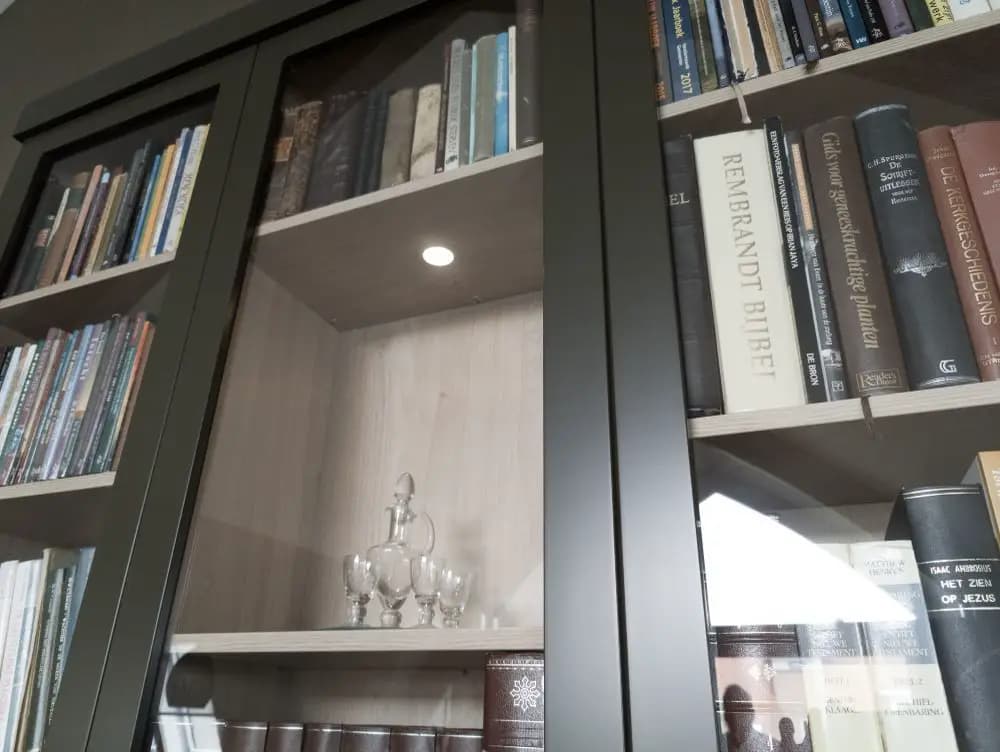 Close-up van op maat gemaakte boekenkast met glazen deuren en houtdecor interieur in Barneveld.