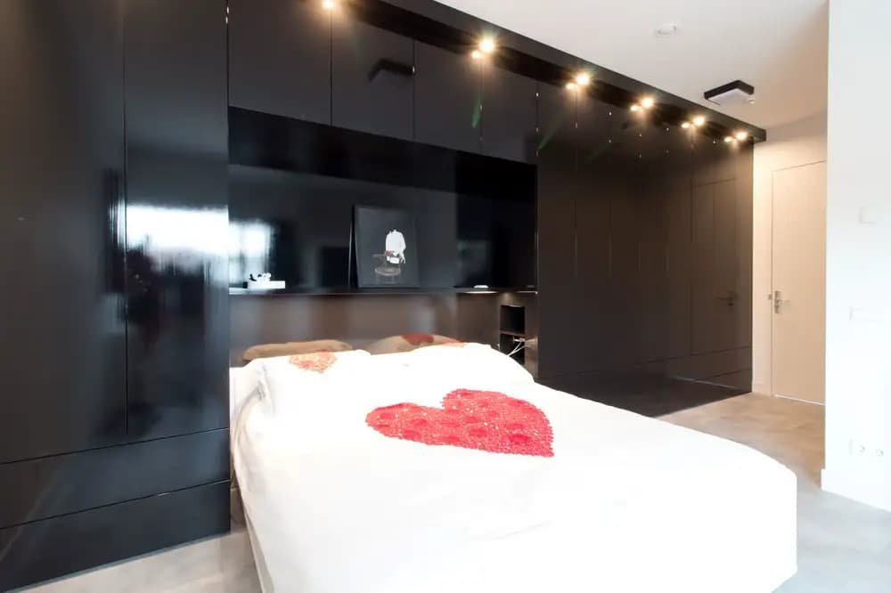 Ingebouwde zwarte hoogglans kledingkast met spotluifel verlichting en bedachterwand in Ede.