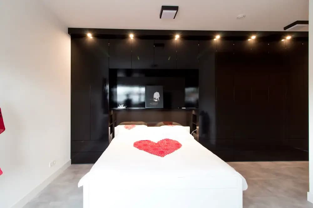 Wandvullende kledingkast in zwarte hoogglans rondom bed in Ede.