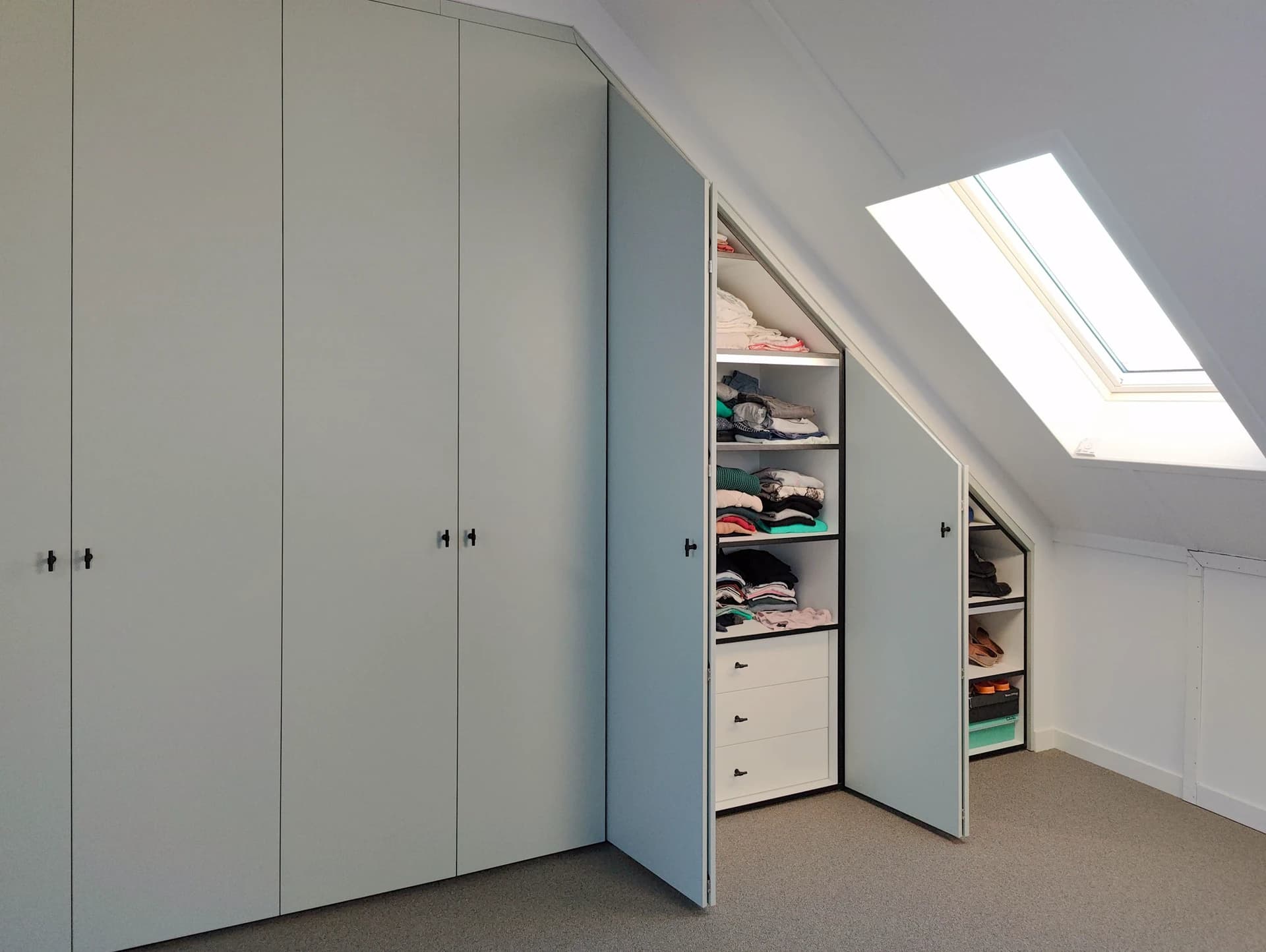 Ingebouwde kledingkast met geopende vouwdeuren onder schuin dak in Nijkerk.