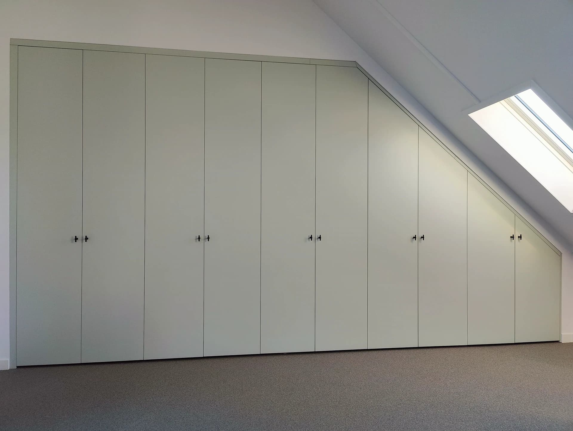 Ingebouwde kledingkast met vouwdeuren onder een schuin dak in moderne slaapkamer.