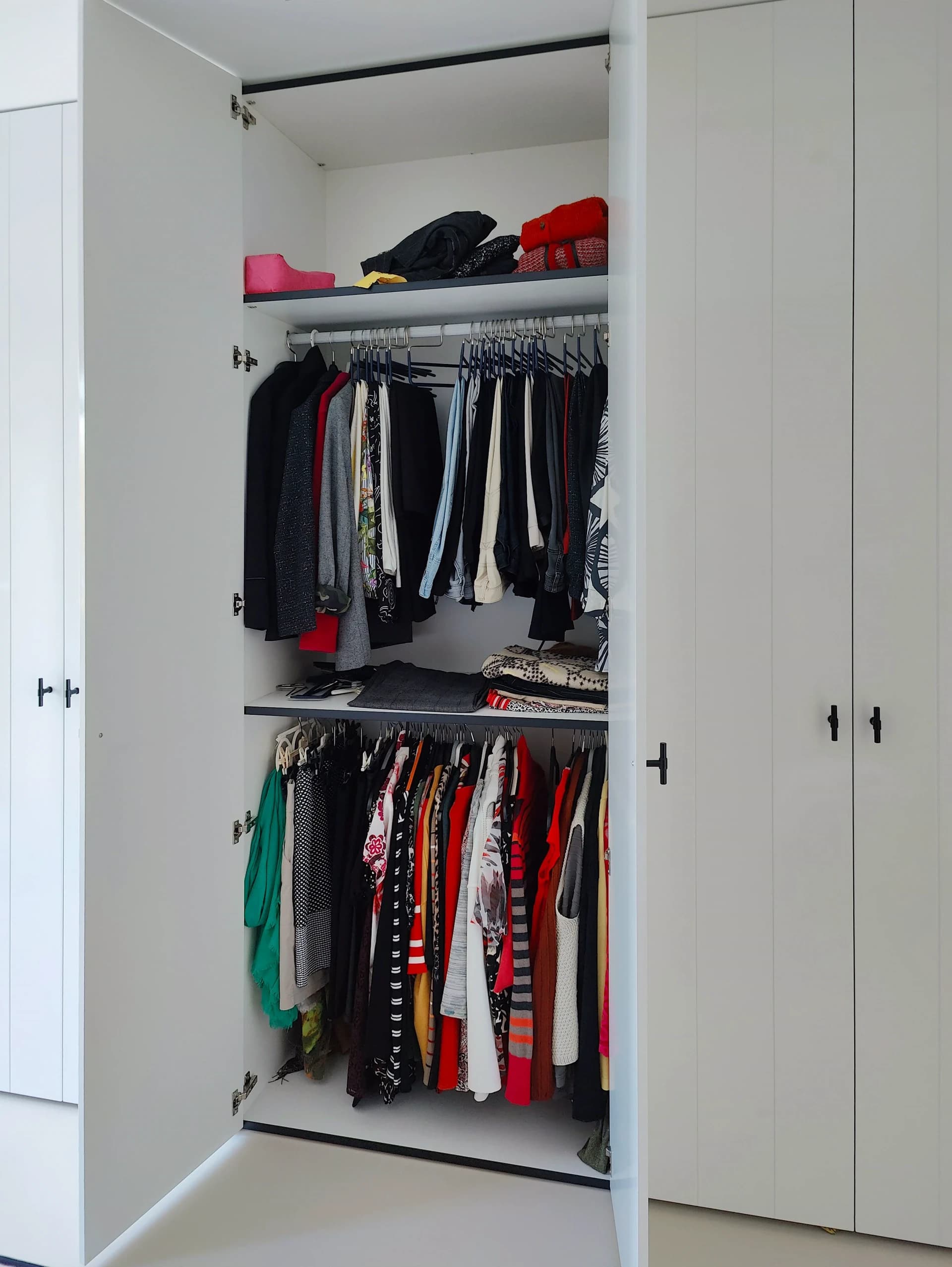 Hoogglans witte kledingkast met opbergvakken en kleding netjes opgeborgen.