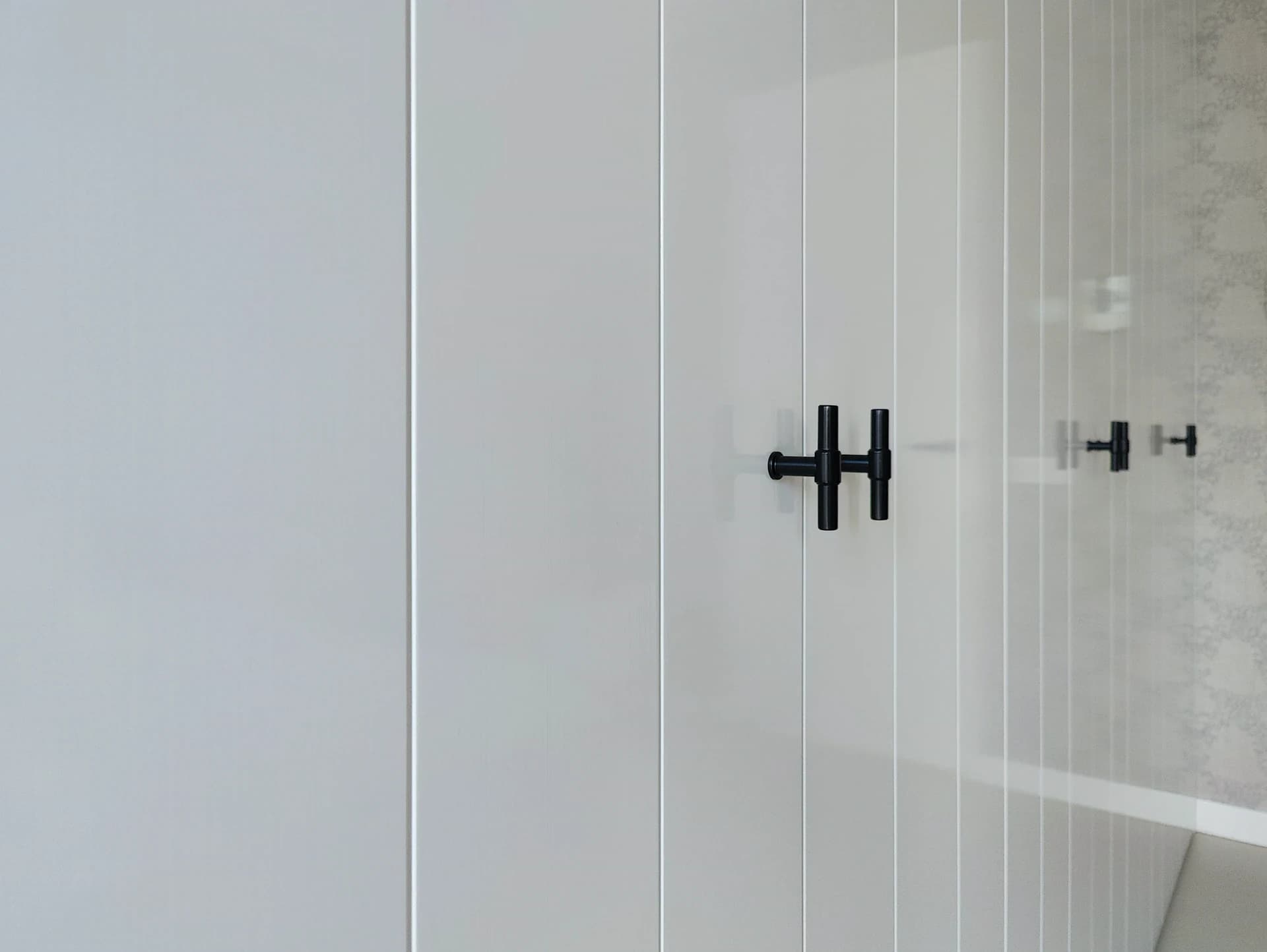 Detail van de kastdeuren met matte zwarte handgrepen tegen een hoogglans witte afwerking.