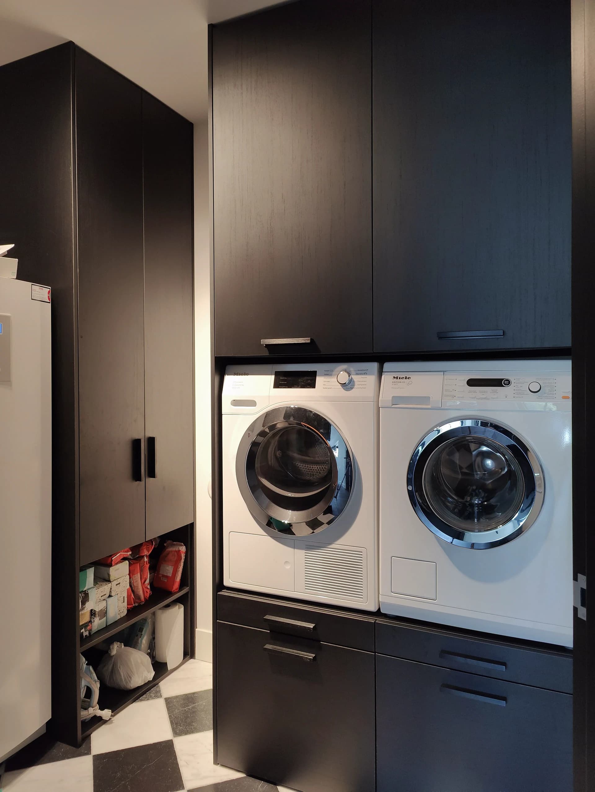 Wasmachinekast met zwarte houtlook decorplaat en opbergruimte in moderne bijkeuken.