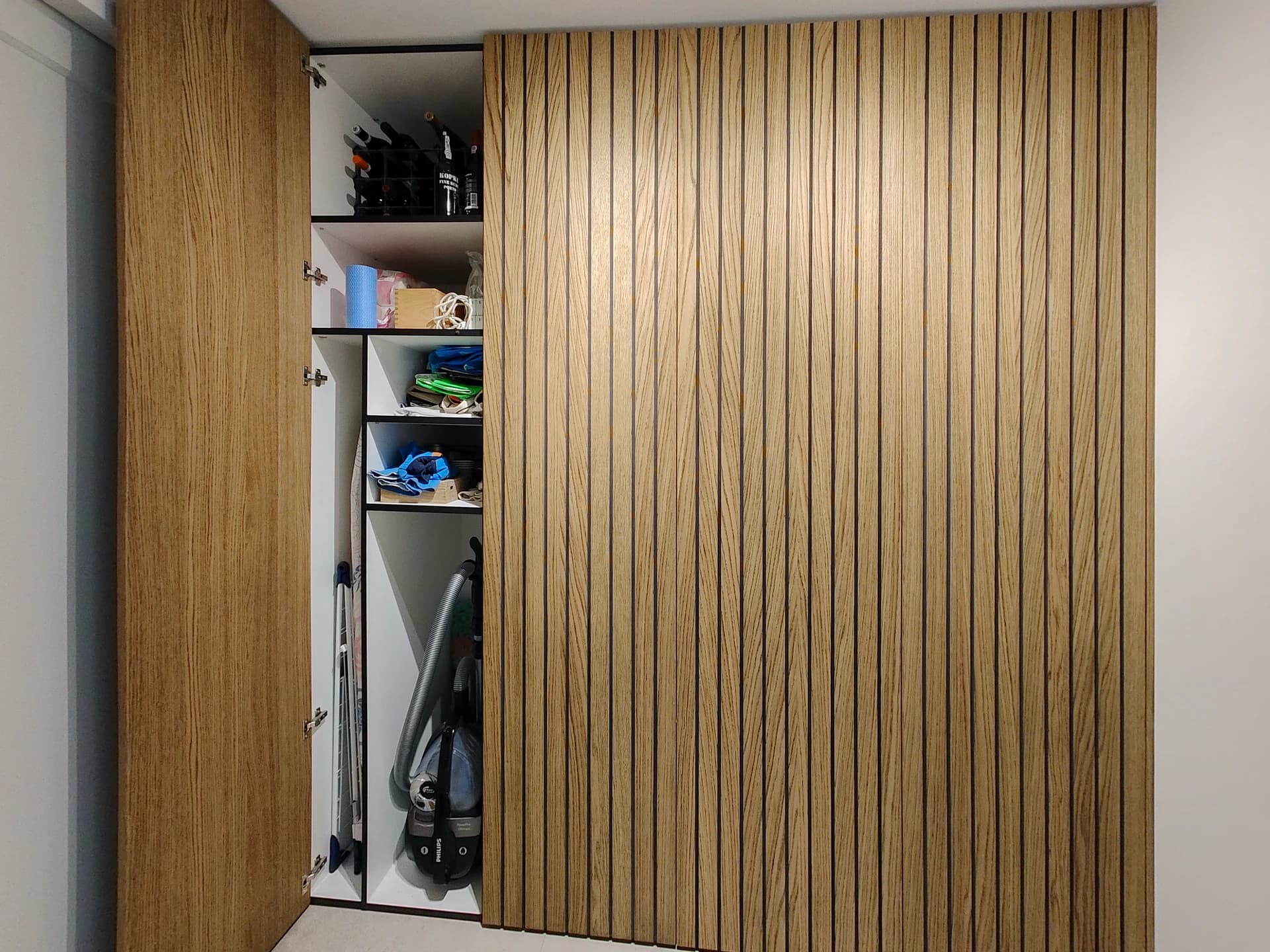 Open bijkeukenkast met ingebouwde wasmachines en opbergruimte, lattenbekleding.