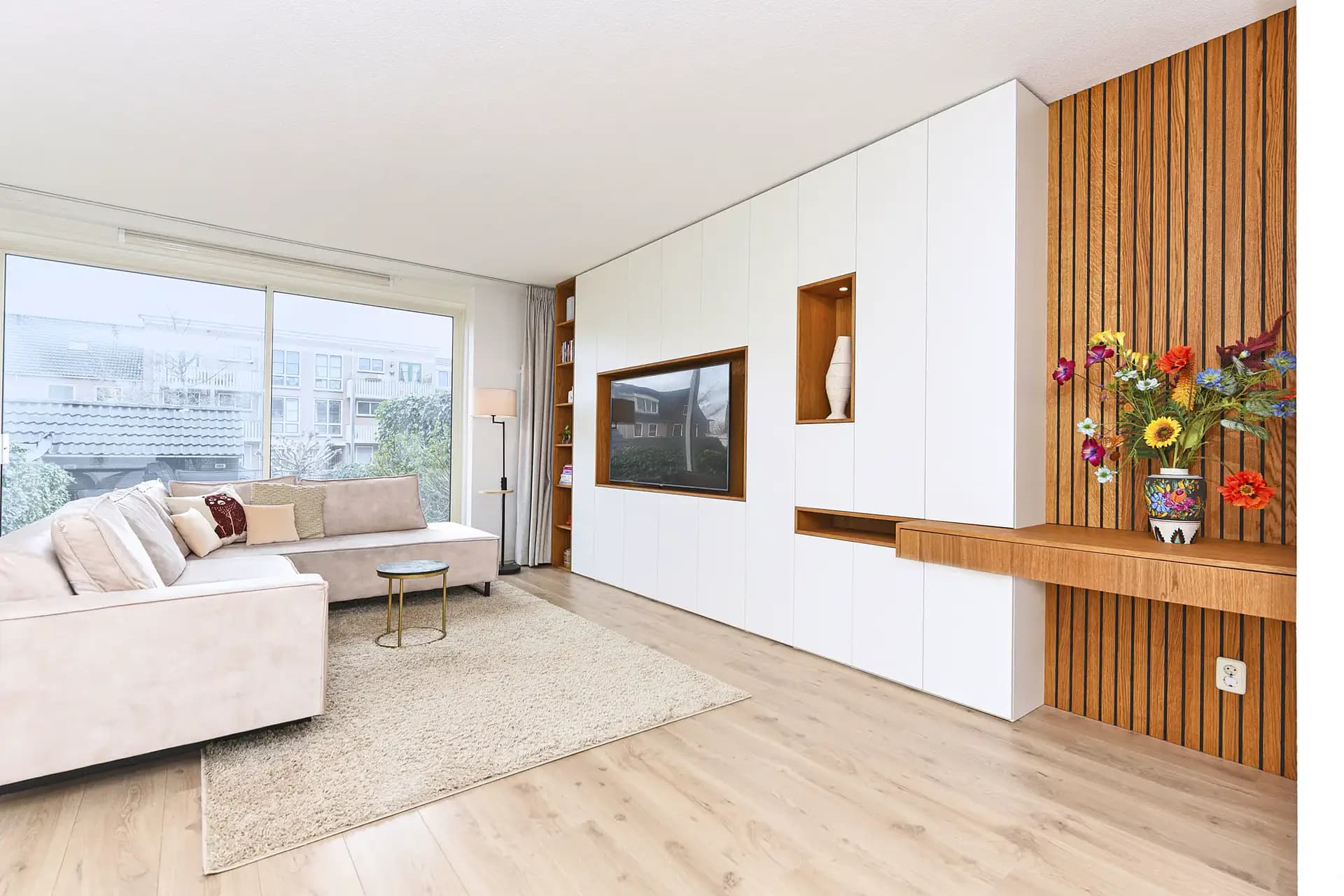 Maatwerk wandkast met ruimte voor TV en nissen met eiken afwerking in een moderne woonkamer in Amersfoort.